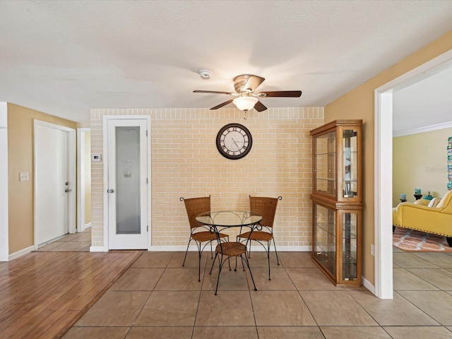 tiled dining space with a textured ceiling, ceiling fan, and brick wall