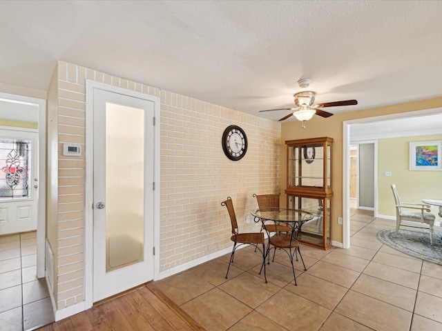 dining area with ceiling fan, light tile patterned floors, and brick wall