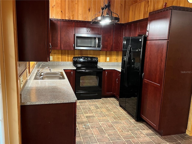 kitchen with wooden walls, sink, black appliances, and decorative light fixtures