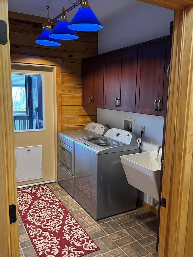 laundry room with wood walls, washer and clothes dryer, cabinets, and sink