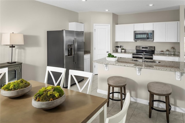 kitchen with a kitchen bar, light stone countertops, white cabinets, and appliances with stainless steel finishes