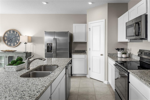 kitchen featuring sink, light tile patterned floors, light stone counters, white cabinets, and appliances with stainless steel finishes