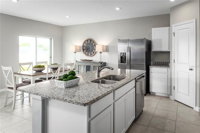 kitchen featuring sink, light tile patterned floors, light stone countertops, appliances with stainless steel finishes, and an island with sink