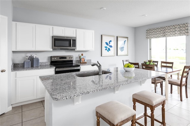 kitchen featuring a kitchen bar, stainless steel appliances, sink, light tile patterned floors, and white cabinets