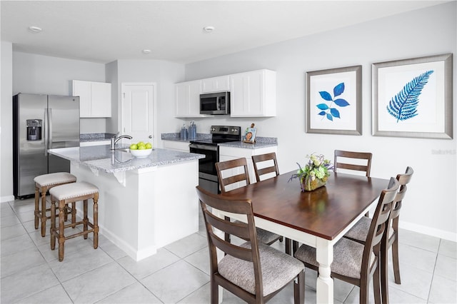 kitchen with an island with sink, light tile patterned flooring, light stone counters, white cabinetry, and stainless steel appliances