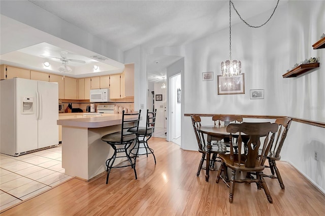 kitchen with kitchen peninsula, light wood-type flooring, ceiling fan with notable chandelier, white appliances, and cream cabinetry