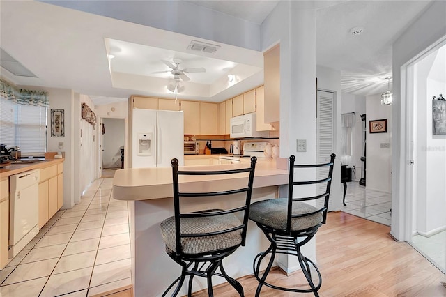 kitchen with white appliances, a kitchen breakfast bar, ceiling fan, a tray ceiling, and light hardwood / wood-style floors