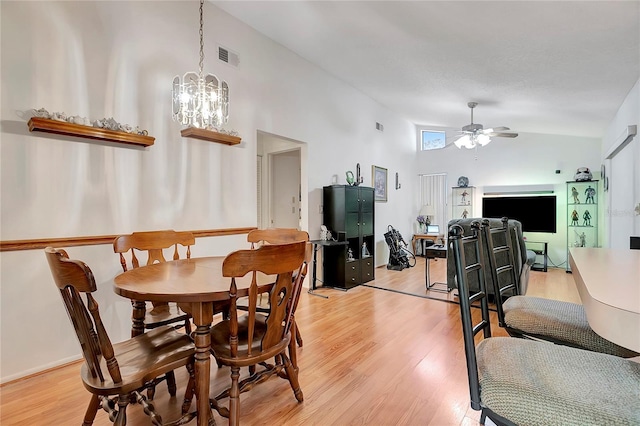 dining room featuring ceiling fan with notable chandelier, light hardwood / wood-style floors, and high vaulted ceiling