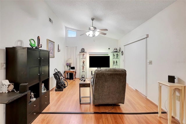 living room featuring ceiling fan, light hardwood / wood-style floors, a textured ceiling, and vaulted ceiling