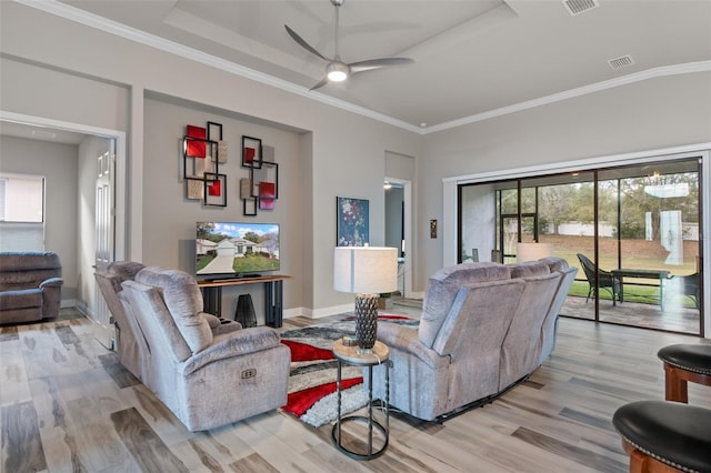 living room with ceiling fan, a raised ceiling, light wood-type flooring, and crown molding