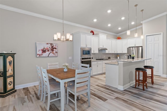 kitchen with a center island with sink, white cabinets, crown molding, light stone counters, and stainless steel appliances