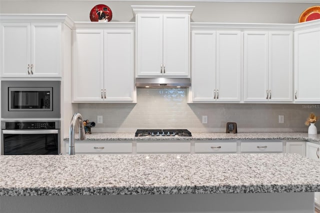 kitchen featuring white cabinets, light stone counters, stainless steel appliances, and tasteful backsplash