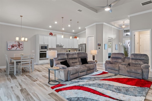 living room featuring ceiling fan with notable chandelier, light wood-type flooring, ornamental molding, and a high ceiling