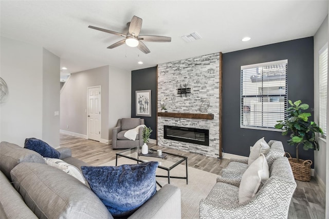 living room with a stone fireplace, ceiling fan, and light hardwood / wood-style floors