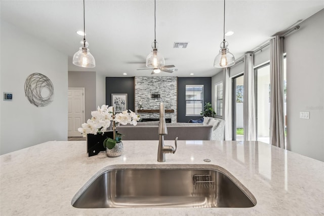 kitchen with pendant lighting, light stone counters, ceiling fan, and sink