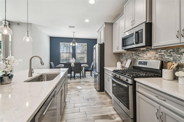 kitchen with light stone counters, sink, hanging light fixtures, and appliances with stainless steel finishes