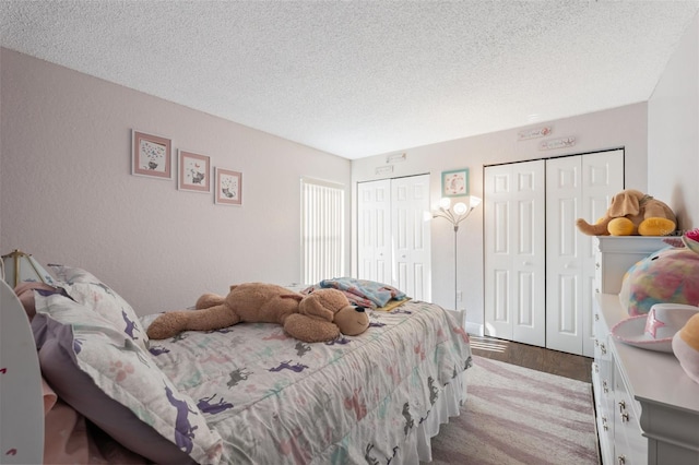 bedroom with a textured ceiling, light hardwood / wood-style flooring, and multiple closets