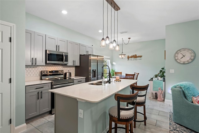 kitchen with sink, stainless steel appliances, gray cabinets, and an island with sink