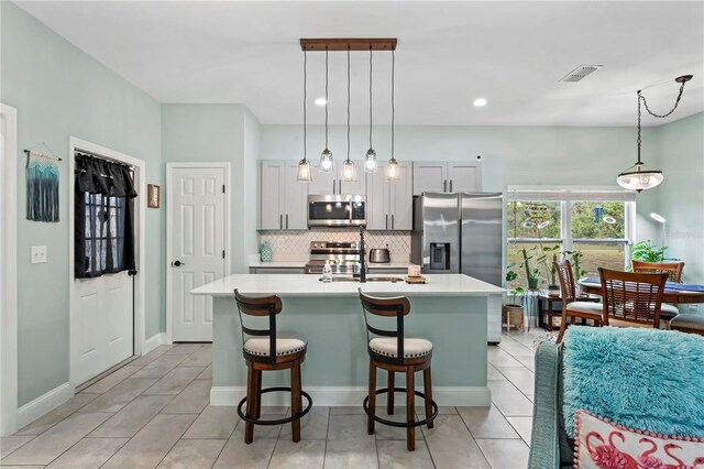 kitchen with a center island with sink, a kitchen breakfast bar, sink, hanging light fixtures, and appliances with stainless steel finishes