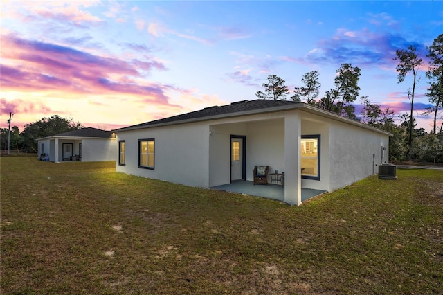 back house at dusk with central AC, a patio area, and a lawn