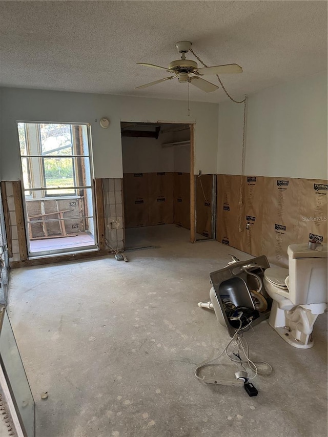 interior space with a textured ceiling, toilet, and ceiling fan