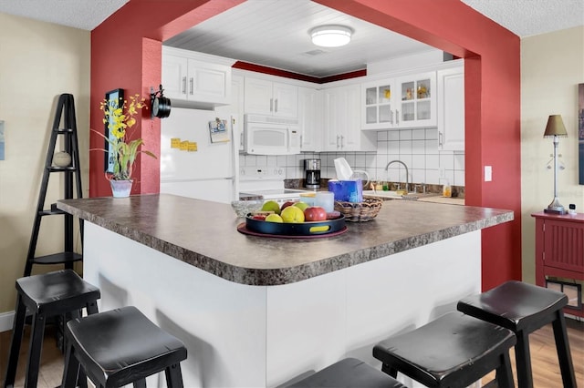 kitchen featuring white appliances, kitchen peninsula, decorative backsplash, white cabinetry, and a breakfast bar area