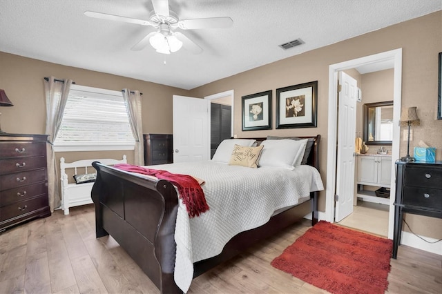 bedroom featuring a textured ceiling, ensuite bathroom, light hardwood / wood-style flooring, and ceiling fan