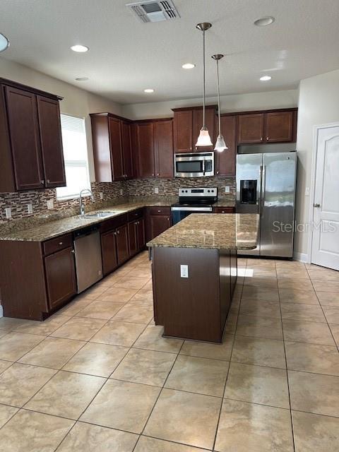 kitchen with stainless steel appliances, sink, pendant lighting, dark stone countertops, and a center island