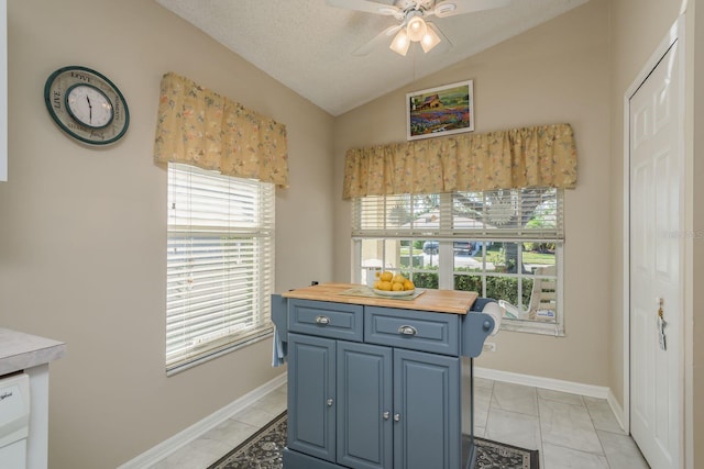 kitchen featuring blue cabinets, vaulted ceiling, a wealth of natural light, butcher block countertops, and light tile patterned flooring