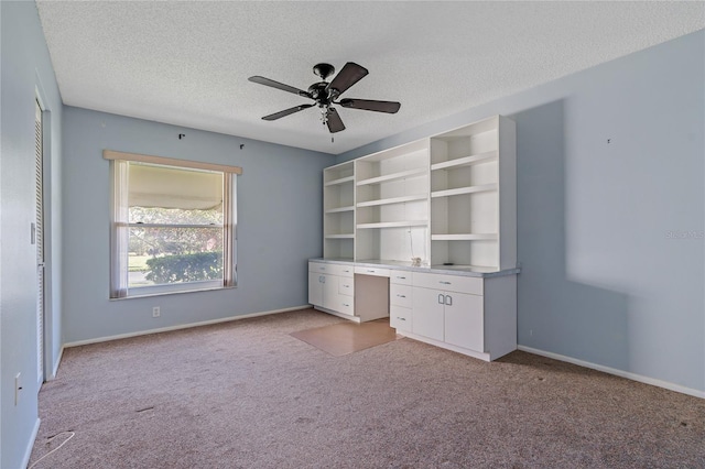 unfurnished office with built in shelves, light carpet, ceiling fan, and a textured ceiling