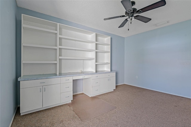 unfurnished office featuring ceiling fan, built in desk, light colored carpet, and a textured ceiling