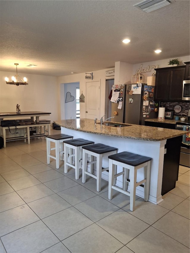 kitchen with appliances with stainless steel finishes, stone countertops, an inviting chandelier, and a kitchen breakfast bar