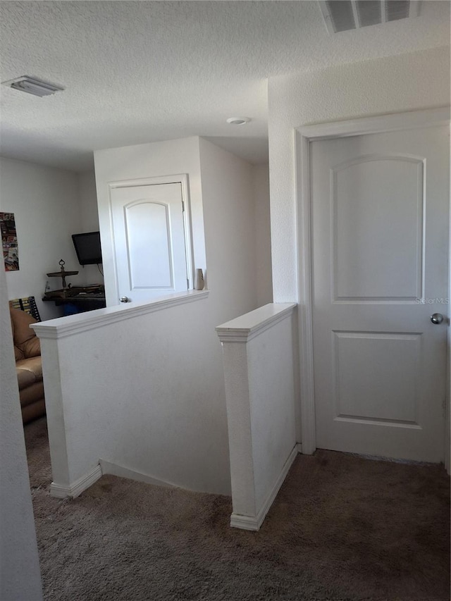 hallway featuring a textured ceiling and dark carpet