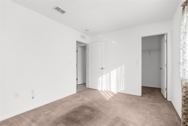 unfurnished bedroom featuring a walk in closet, light carpet, and a closet