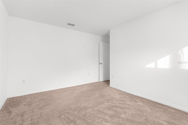 carpeted spare room featuring a textured ceiling, visible vents, and baseboards