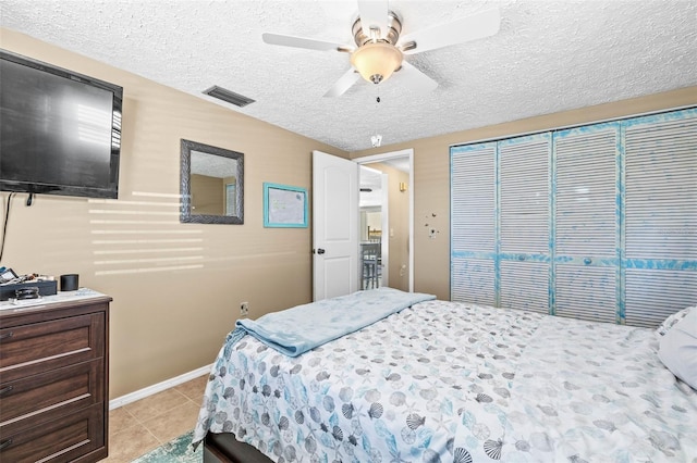 bedroom with ceiling fan, a closet, light tile patterned floors, and a textured ceiling