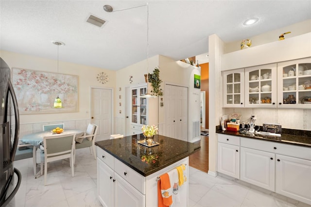 kitchen with hanging light fixtures, white cabinetry, a kitchen island, and refrigerator