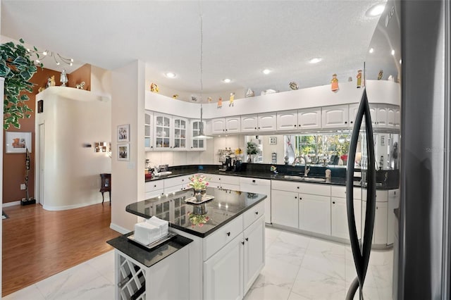 kitchen with a kitchen island, white cabinetry, sink, black fridge, and a textured ceiling