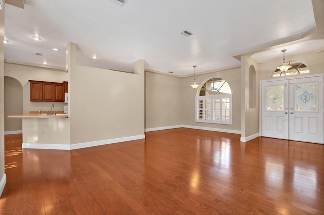 unfurnished living room featuring sink, dark hardwood / wood-style flooring, french doors, and crown molding