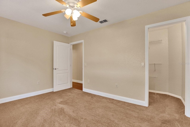 unfurnished bedroom with ceiling fan, light colored carpet, a closet, and a walk in closet