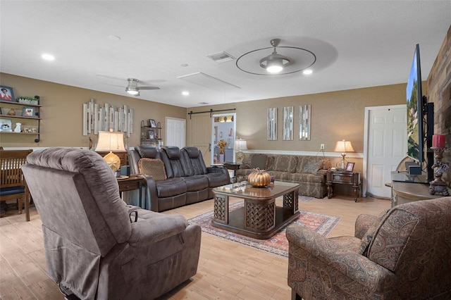 living room with a barn door, light hardwood / wood-style flooring, and ceiling fan