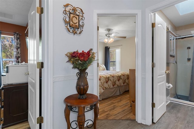 hallway featuring a textured ceiling, light wood-type flooring, and a skylight