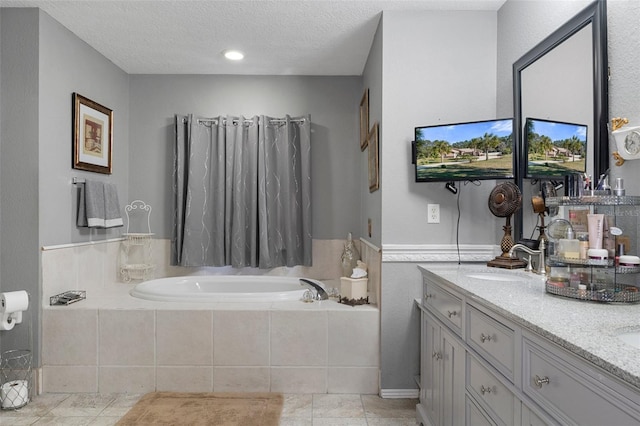 bathroom with tile patterned flooring, a textured ceiling, vanity, and tiled bath