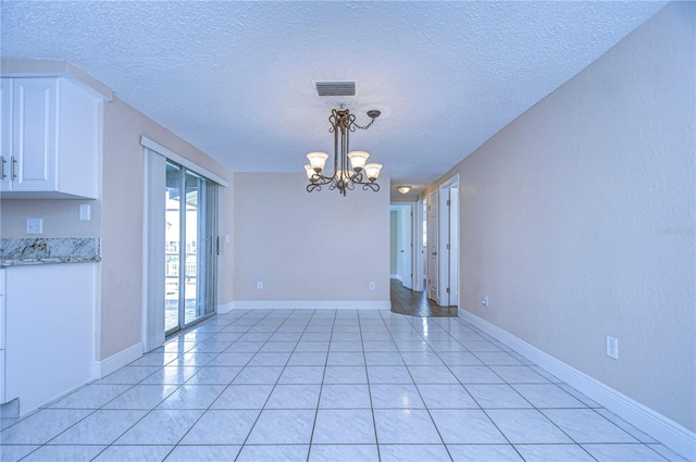 unfurnished dining area featuring light tile patterned floors, a textured ceiling, and a chandelier