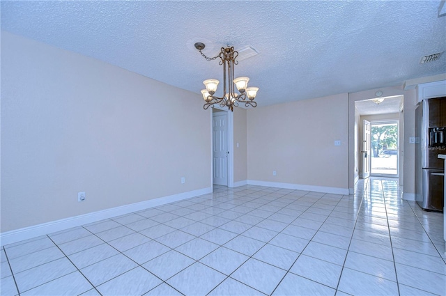 tiled spare room featuring a textured ceiling and an inviting chandelier