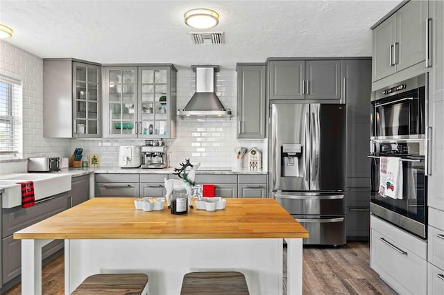 kitchen featuring stainless steel refrigerator with ice dispenser, gray cabinets, tasteful backsplash, and wall chimney exhaust hood