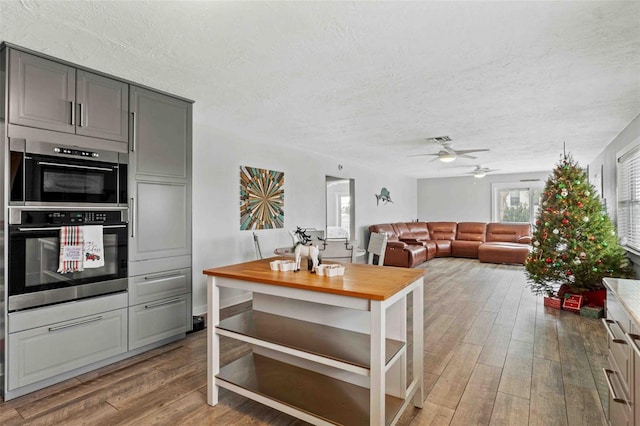 kitchen with a textured ceiling, double oven, ceiling fan, hardwood / wood-style floors, and gray cabinets