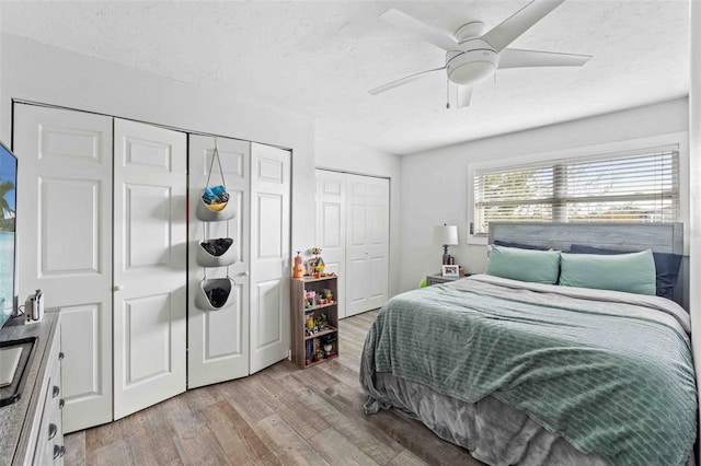 bedroom featuring ceiling fan, light hardwood / wood-style floors, and two closets