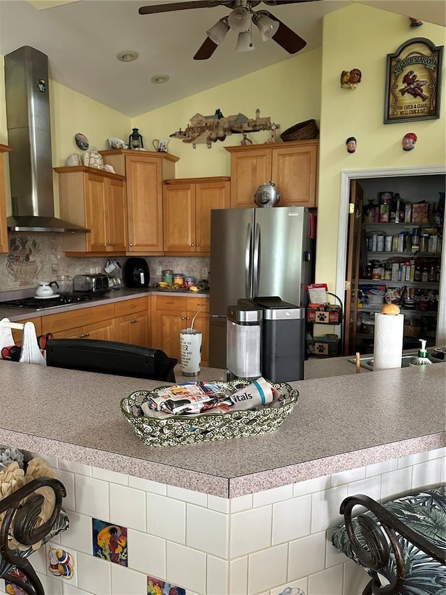 kitchen featuring wall chimney range hood, stainless steel refrigerator, ceiling fan, gas stovetop, and decorative backsplash