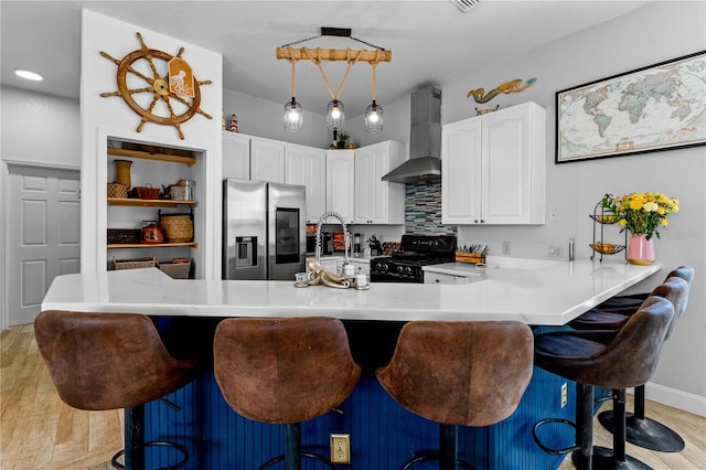 kitchen with wall chimney exhaust hood, stainless steel fridge, black gas range oven, and a breakfast bar area